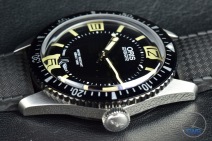 Oris Divers Sixty-Five closeup sitting on black leather with its crown in view [01 733 7707 4064-07 4 20 18]
